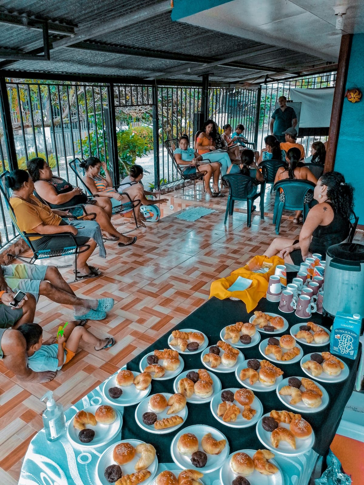 Mesas largas servidas con platos de comida para un almuerzo comunitario, con personas sentadas alrededor del salón