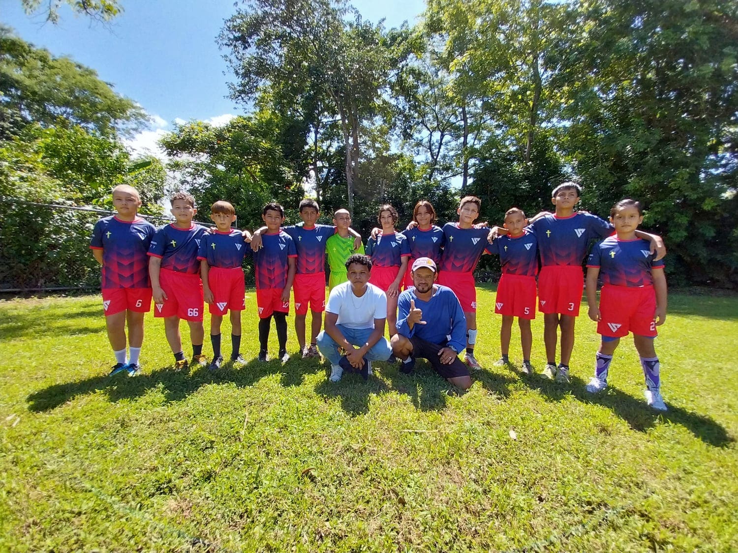 El equipo de fútbol del club de niños, en uniforme rojo y azul, posa en fila sobre la cancha de césped